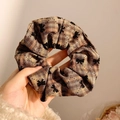Chouchou en tissu à carreaux marron avec motif de nœud noir tenu dans la main - Imprimé nœud à carreaux / Marron