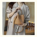 Brown leather bucket bag with plaid silk scarf and shoulder strap held by a model - Biscuit