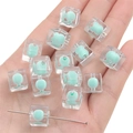Hand hält dreizehn minzgrüne Makronen-Acrylwürfelperlen für DIY-Schmuckherstellung - 10 Stück/Packung / Transparentes Grün