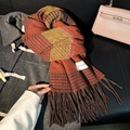 Orange and brown plaid winter scarf with tassels displayed on a leather sofa backdrop - Orange