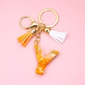 Detail of letter Y resin keychain with gold leaf, orange and white tassels on pink background - Letter Y