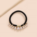 Macro view of black elastic hair tie with curved gold alloy bar and varied size white pearls - Pearl Arc Style