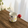 Keramiktasse mit bunten Punkten und großem rotem Kugelgriff auf rustikalem Holztisch - Punktmuster Kugelgriff