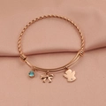 Detalle de brazalete rígido de oro rosa con colgantes de ángel, lazo y gema azul - Oro rosa