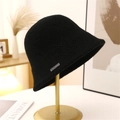Detailed shot of a black knit bucket hat with silver metal logo on a gold display stand - M (56-58cm) / Black