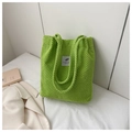 Detail of green corduroy tote bag with grey label on white bed with soft lighting - Kiwi Green