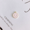 Detailed macro of a round pink enamel G letter pendant with golden metal edging and ring - Letter G