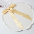 Barrette à cheveux double nœud en satin jaune clair avec de longs rubans sur un plateau blanc - Jaune