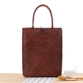 Bolso de ratán trenzado marrón con textura clara y cierre de botón en mesa de madera - Color Madera Antigua