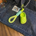 Close-up of green mini clog keychain with yellow and blue braided cord on denim - Dopamine Green