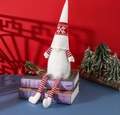 Vue détaillée d'un gnome de Noël en peluche assis sur des livres anciens au décor festif - Poupée sans visage à longues jambes / Blanc