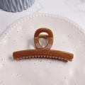 Top view of amber resin hair claw clip with gold spring on a textured decorative plate - Solid Caramel - Butterfly Buckle Straight (Approx 11.3cm)