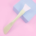 Detailed view of dual-ended silicone face mask brush with scraper on a blue stand - Green