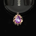 Macro view of a purple teardrop crystal pendant set in a golden lace hollow metal base - Light Purple