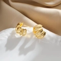 Detalle macro de pendientes dorados con ondas sobre seda beige y cerámica - 24K / Dorado
