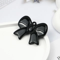 Macro shot of a glossy black bow-knot charm with hanging hole on a white tray - Black