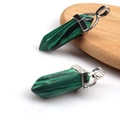 Polished malachite hexagonal column pendant with silver metal clasp on a wooden surface - Malachite