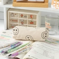Beige corduroy pencil case with smiley face design and colorful cartoon pens on a desk - Beige Heart-Eye Pencil Case