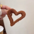 Gros plan d'une pince à cheveux en peluche marron en forme de cœur tenue par une main - Marron