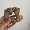Hand holding a khaki PU leather scrunchie with pleated texture on white background - Normal Version / Milk Tea