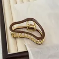 Elegant gold metal hair claw with dark brown wavy finish on a jewelry tray - Milk Coffee
