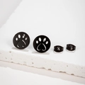 Close-up of matte black hollow cat paw and heart earrings on a white stone base - Round Paw Print Shape (689) / Black