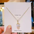 Élégant collier doré avec pendentif gland en perle blanche sur une carte chic - Petite Perle de Sirène