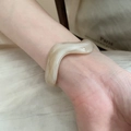 Vista macro de pulsera rígida acrílica ondulada con patrón de mármol crema en la muñeca - Beige Crema (Café Claro) / 【atributos Del Producto】: Visualmente Se Trata De Una 【pulsera Ancha Y Ondulada】 Con Un Tono De Color General De 【beige Crema】 Y Textura De Mármol Natural O Efecto De Arena Movediza De Resina.