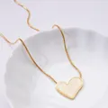 Detailed close-up of a gold heart pendant necklace with white shell inlay on a white plate - Beige Heart