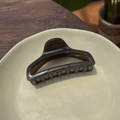 Dettaglio della grande pinza per capelli marrone scuro traslucida su un piatto di ceramica - grigio scuro