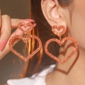 Makroaufnahme großer geschichteter Herzohrringe mit glitzernden Kristallen in Roségold - Doppelherz-Ohrstecker / Orange