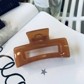 Close-up of a large amber resin hair claw clip with a hollow rectangular design on a book - Translucent Dark Orange