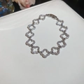 Macro shot of silver clover bracelet with sparkling pave zircon on white leather - Four-leaf Clover / Silver