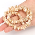 Handheld view of irregular natural shell beads in cream white with brown texture - Irregular Natural