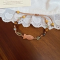 Detailansicht eines geflochtenen Armbands mit Holzperlen und geschnitztem Fisch auf Holz - Braun-Grün (Holzfisch-Anhänger)