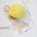 Detail of yellow fluffy ball keychain with pink tassel and colorful resin letter A - Letter A