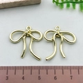 Two 3cm golden hollow bowknot metal pendants for DIY jewelry making shown with a ruler - Small Bowknot - KC Gold (21382)