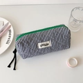 Detailed macro view of black and white checkered quilted pencil case with green zipper detail - Black