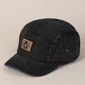 Détail d'une casquette en denim noir avec écusson marron et anneau métallique décoratif - Noir