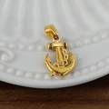 Vue macro d'un pendentif ancre plaqué or avec chaîne sur une assiette en céramique blanche - Ancre / Or