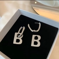 Dettaglio degli orecchini a cerchio lettera B argento in una scatola di velluto nero - 14k / Argento