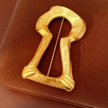 Macro-opname van een vintage gouden sleutelgatbroche met reliëf op bruin fluweel - Goud - Onregelmatige Granulaire Sleutelgatstijl