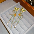 Detail van gouden vlinder oorbellen met groene zirkoon en witte parels aan de ketting - Zilveren Pin - Groene Vlinder Kwastje Oorbellen