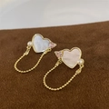 Detailed close-up of heart-shaped shell earrings with pink zircon and gold chain tassels - Shell Heart Clip Earrings Gold