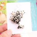 Charming gold-plated frog brooch with black and clear rhinestones on a fashion display card - Black & White