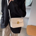 Elegant off-white tofu-style crossbody bag with gold buckle on a stylish model - Beige