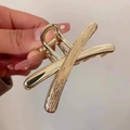 Elegant golden metal cross shark hair claw clip with textured finish shown on hand - Crisscross Streamline / Gold