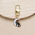 Close-up of black cat on white moon enamel keychain with golden clip on wood surface - White Moon