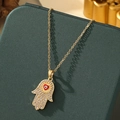 Detailed close-up of golden Hamsa Hand necklace with red heart and evil eye detail - A6-Gold