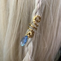 Close-up of golden spiral hair clip with a blue teardrop crystal bead on a braid - Blue Pendant Necklace